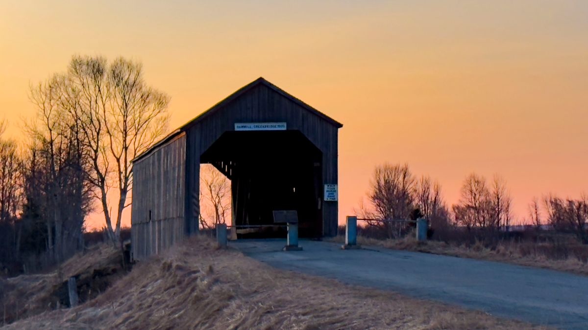 A covered bridge next to a road was taken at sunset in Canada