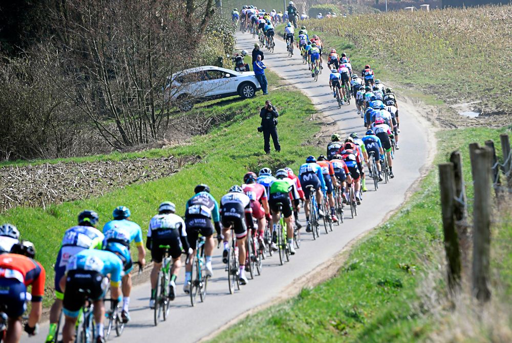 The 2018 Gent-Wevelgem peloton is lined out on a narrow road