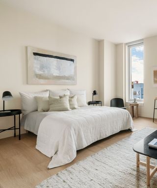 A studio apartment with a large bed, windows, and a textured area rug