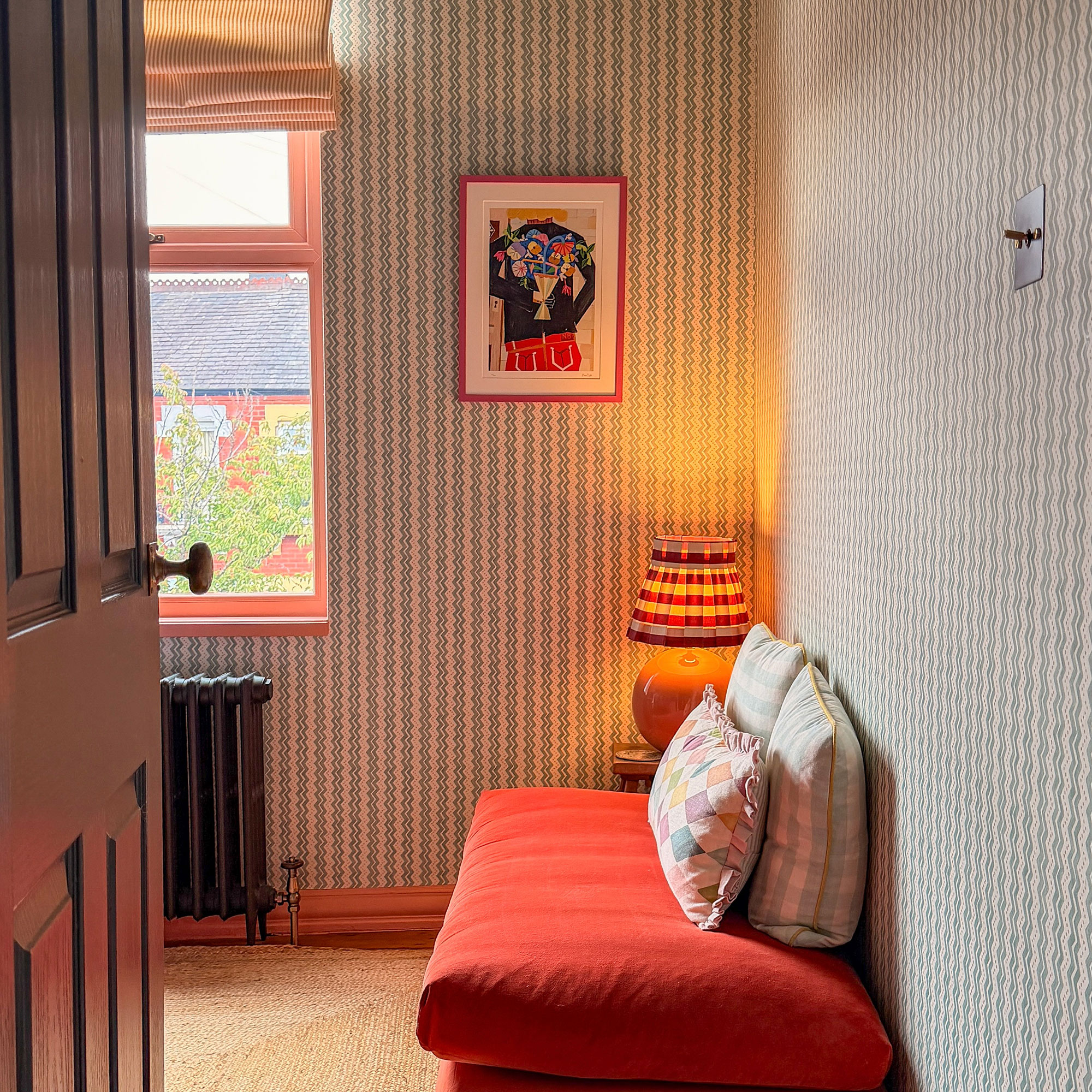 Room with stripy patterned wallpaper, burnt orange futon and framed art on wall