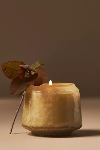 Mottled gold jar holding lit candle and brown leaf leaning against