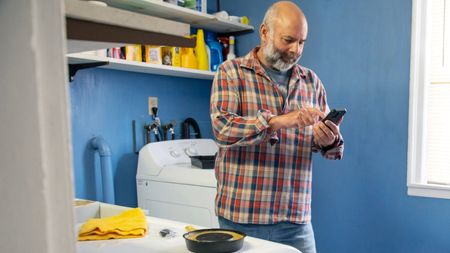 A mature man uses his smartphone while doing DIY in the laundry room