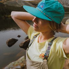 Model basking in the sun wearing a yellow t shirt and teal cap sold at Helly Hansen