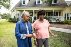 Two women walking in the front yard of a large rural home