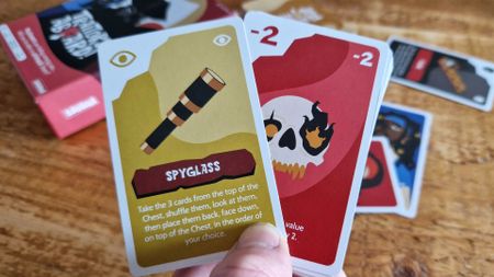 A hand holds up two cards, with more and a box visible in the background lying on a wooden table