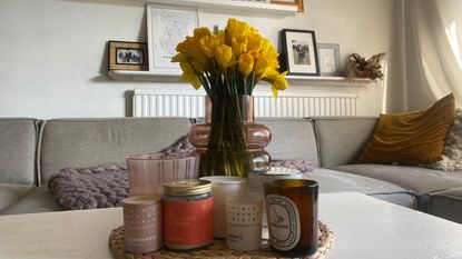 A range of candles sitting on Annie's white wooden coffee table beside a bouquet of daffodils with a gallery wall behind