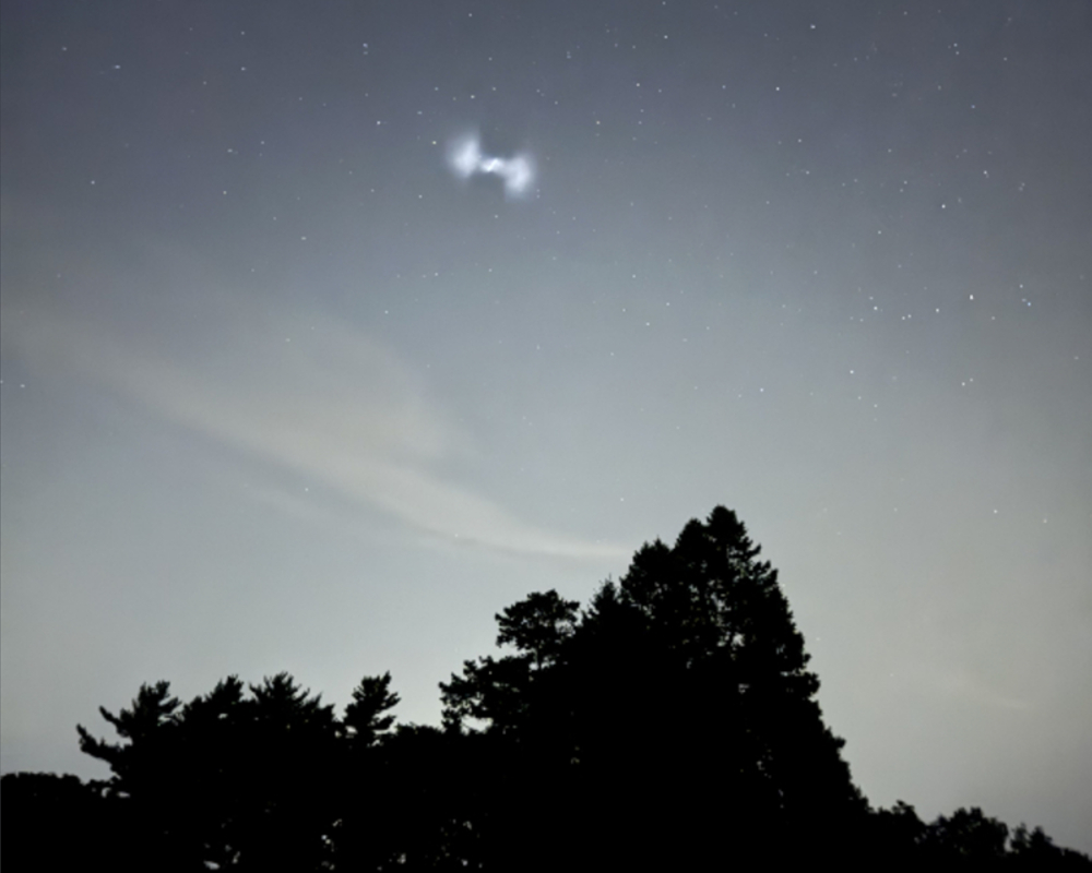 A ghostly white spiral of light in the night sky above some trees
