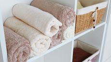 Rolled neutral towels on white shelf with rattan basket