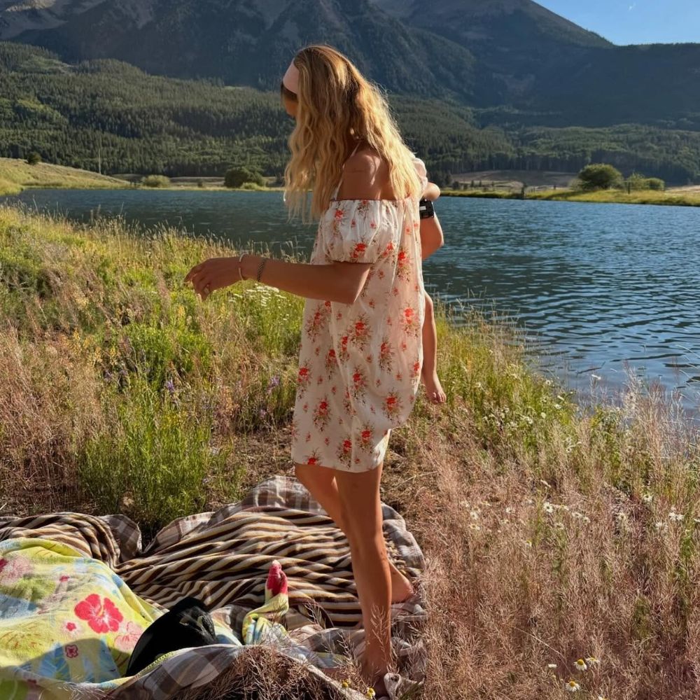 Bella Hadid stands outside by a lake wearing a white cotton floral minidress.