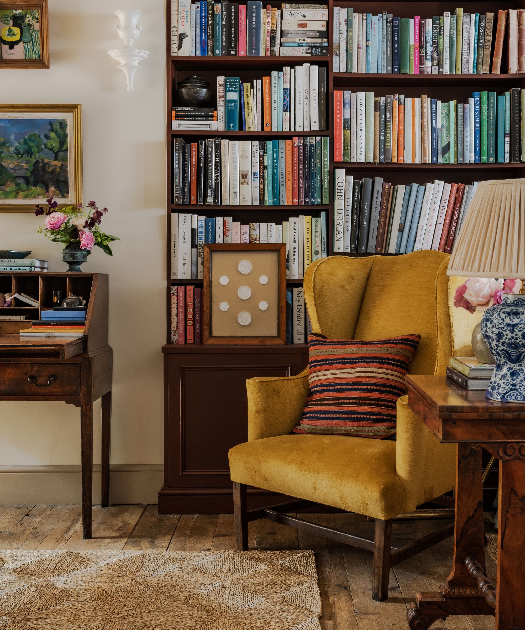 Living room with reading nook in corner, bookshelves, yellow velvet armchair and wood side table with antique ceramic lamp