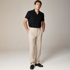 model wears black short sleeve button up top, beige linen trousers, and black loafers