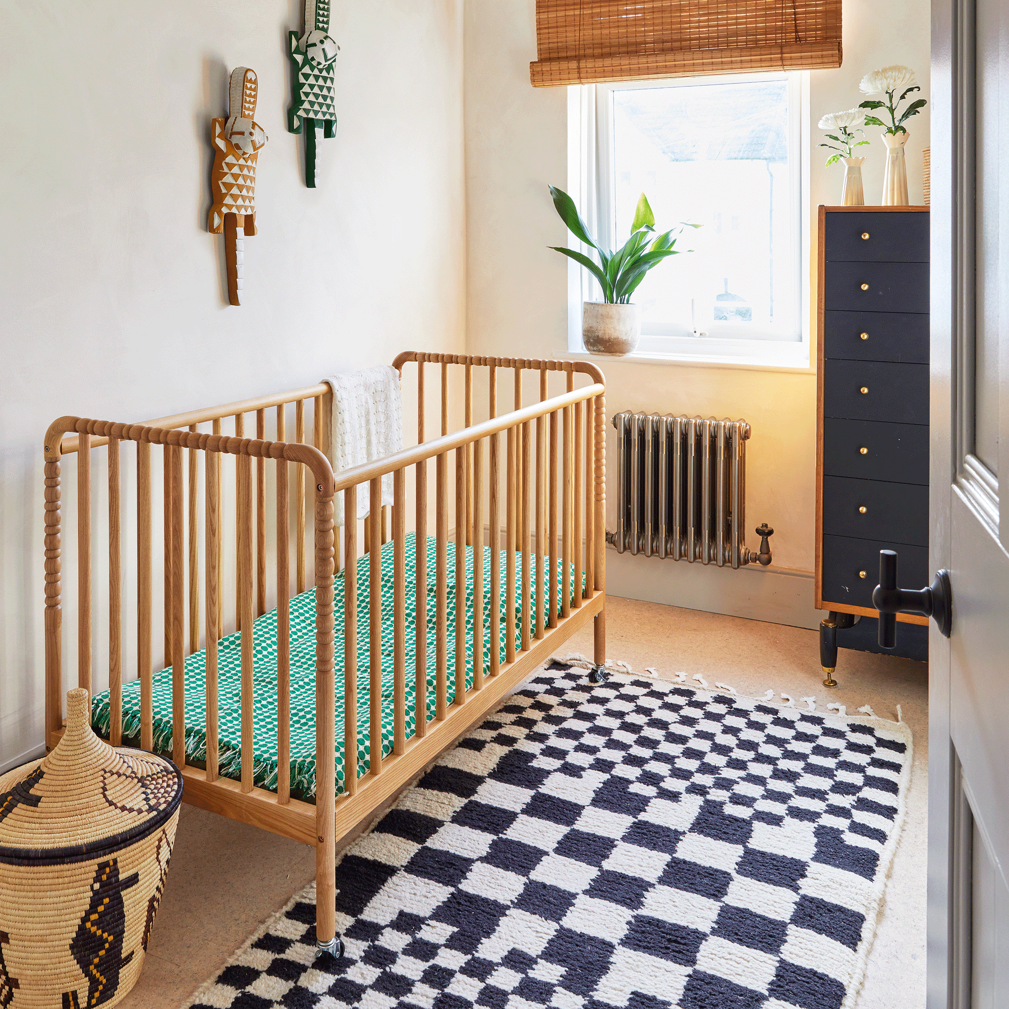 a nursery with a wooden cot and a black and white checked rug