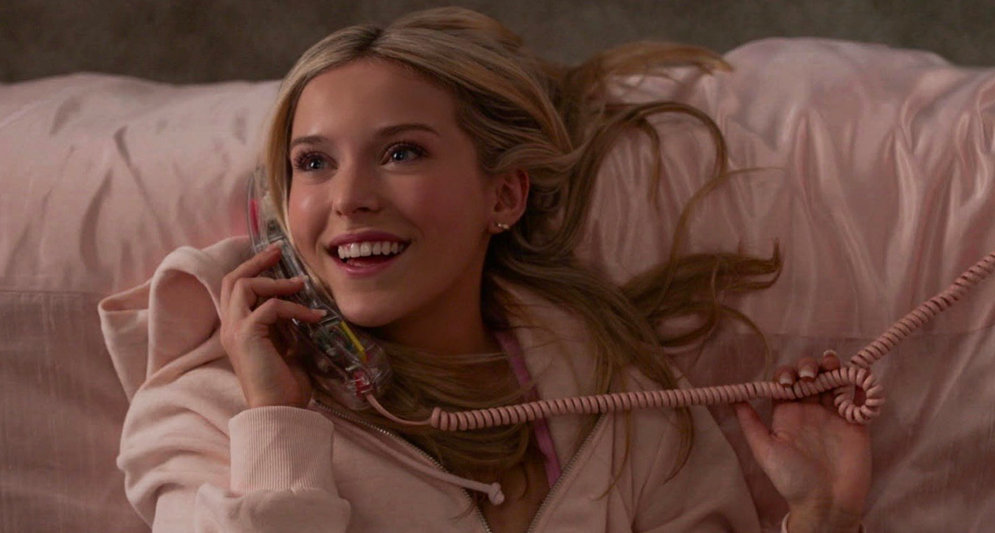 lexi minetree as elle woods talking on the phone wearing pink and lying in a pink bed in a still from the legally blonde prequel elle