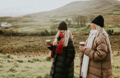 Two young women enjoying a winter walk outdoors, dressed in warm clothing, holding takeaway coffee cups.