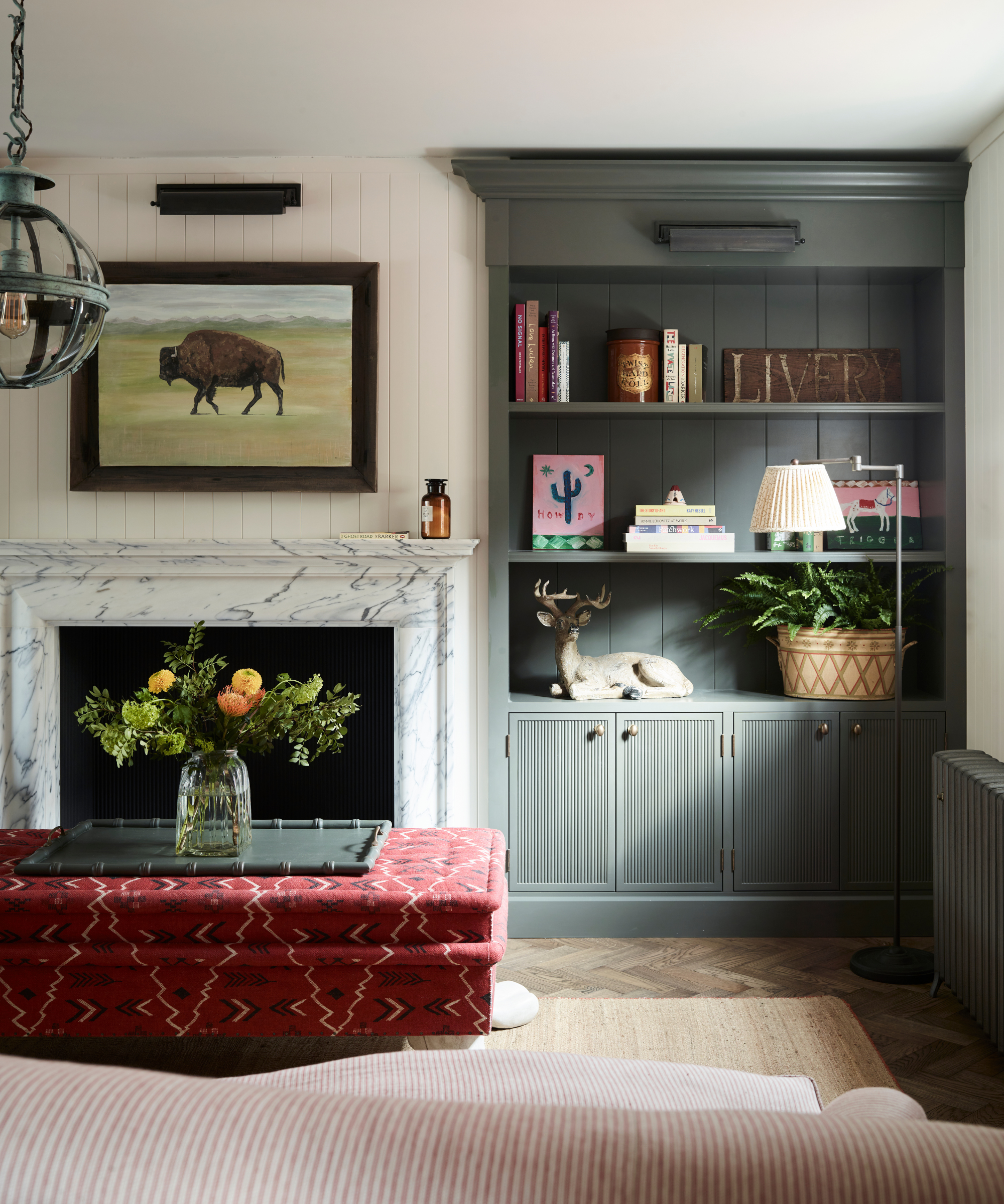a rustic living room with dark gray built-in shelves with decor on them and a red ottoman