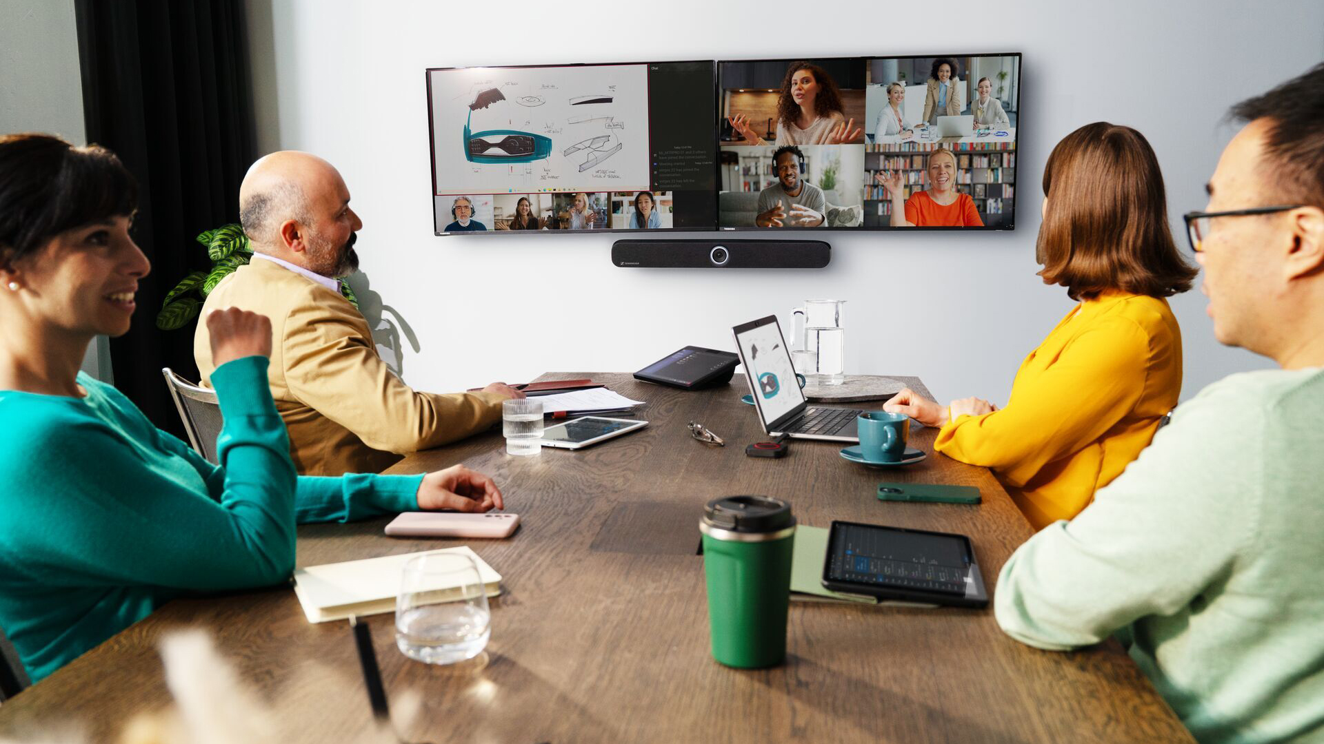 Four people sitting at a boardroom table engaging in a video call with four other people