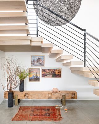 A staircase with 'floating' treads rise over a bench, rug, and framed artwork