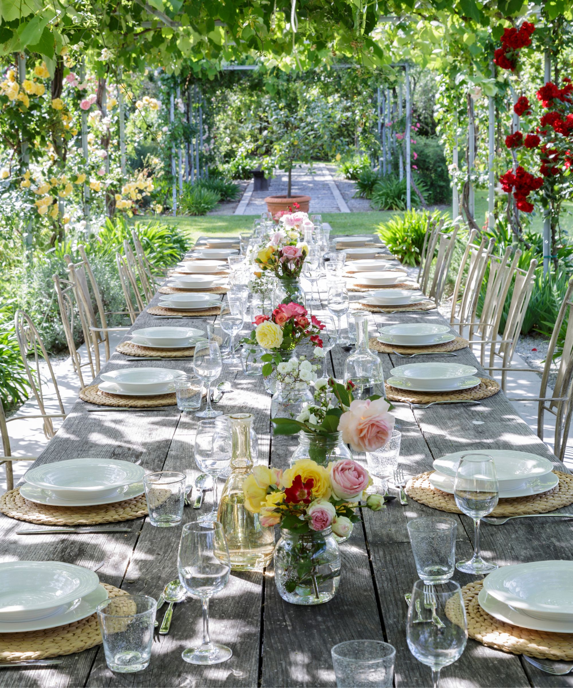 long table outdoors in a pretty garden with vases of flowers dotted along the centre