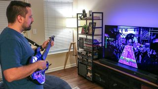 A person playing Rock Band 4 using the PDP Riffmaster in front of a TV