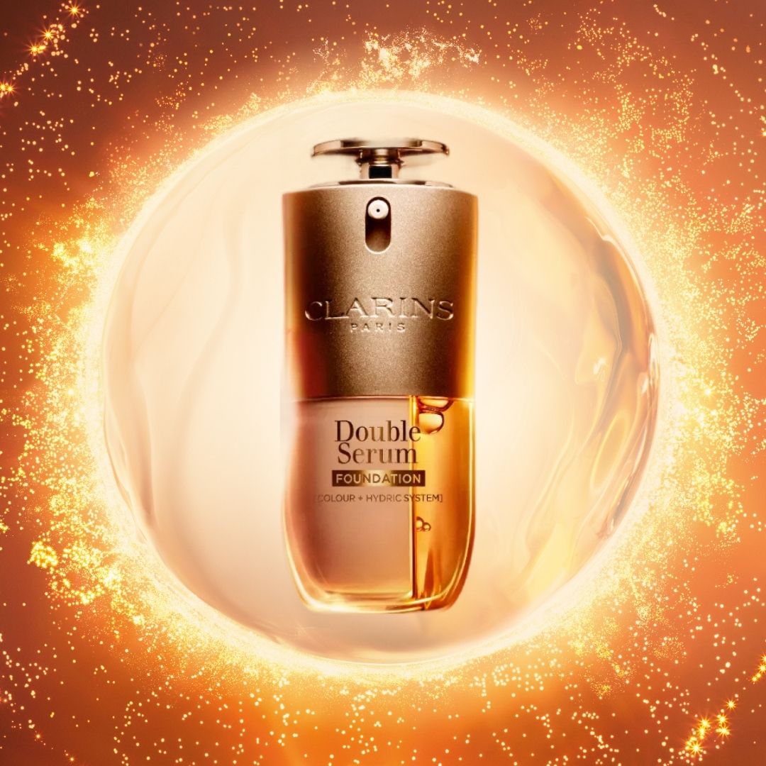 A product picture of the Clarins Double Serum Foundations, surrounded by a circle split into foundation and serum, and fiery, sun-like circles around it/ on a bronze-coloured background