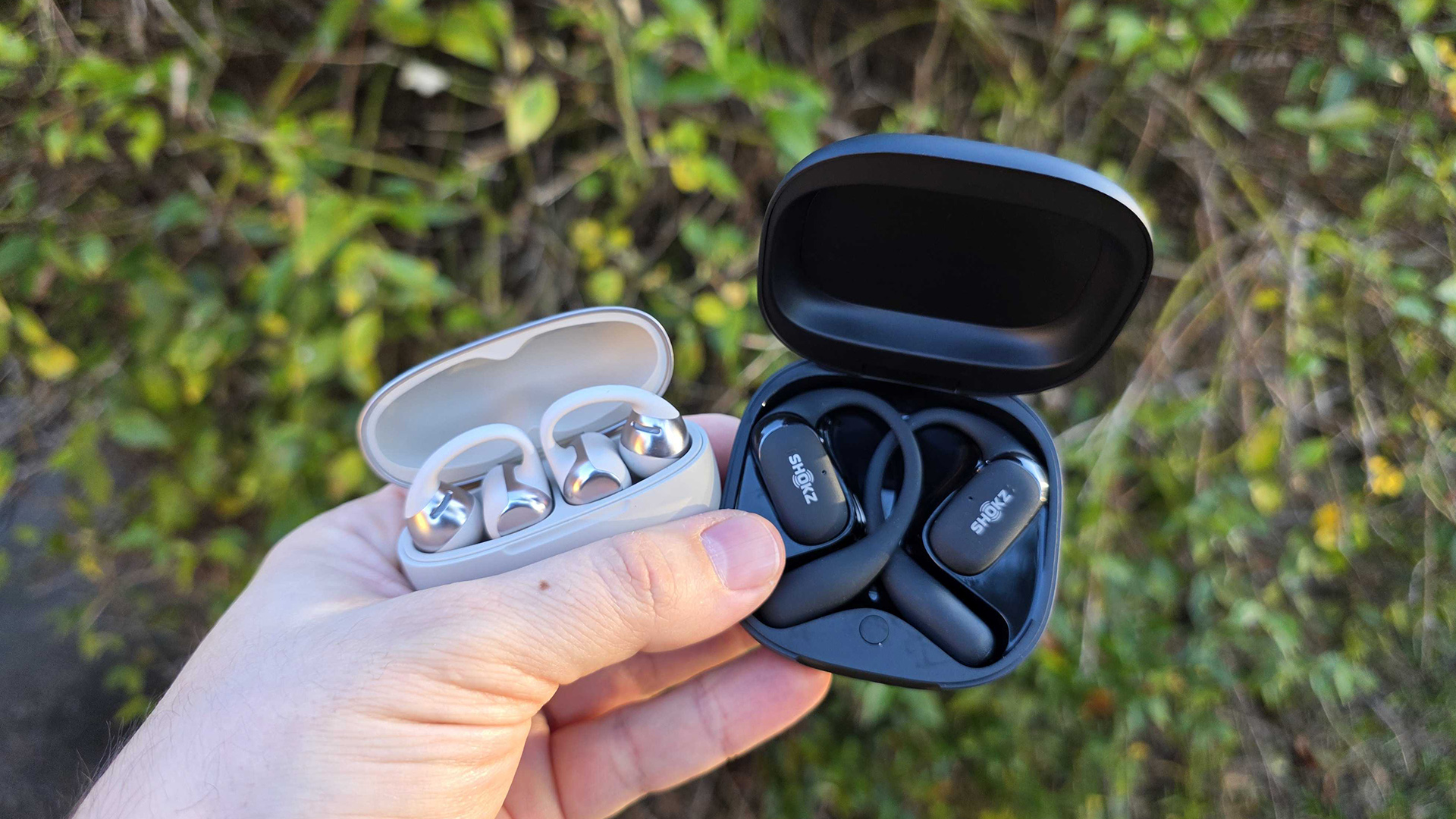 Shokz OpenDots One and OpenFit 2 Plus in hand in front of garden
