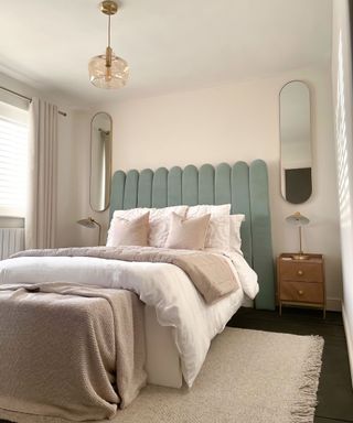 A final 'after' image of DIY scallopped upholstered headboard in bedroom with oblong mirror decor on either side of bed with side tables and curtain window treatment and cream rug