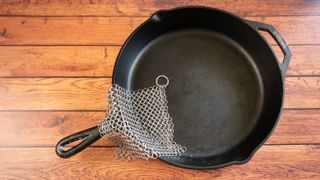 A cast iron skillet with a chainmail scrubber on a wooden surface