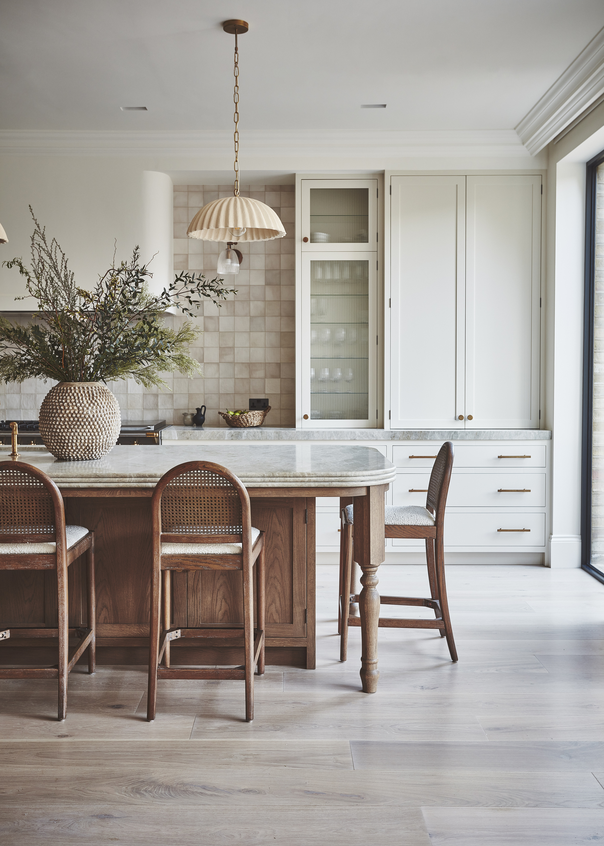 A kitchen with slim cream shaker cabinetry, a large prep table with ogee edges, and a zellige tile backsplash