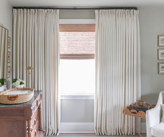 nursery room with gray walls, cream curtains, wooden dresser and corner of white armchair