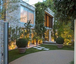 A contemporary modular home with resin bound driveway in front, sympathetically lit with uplighters in the front garden