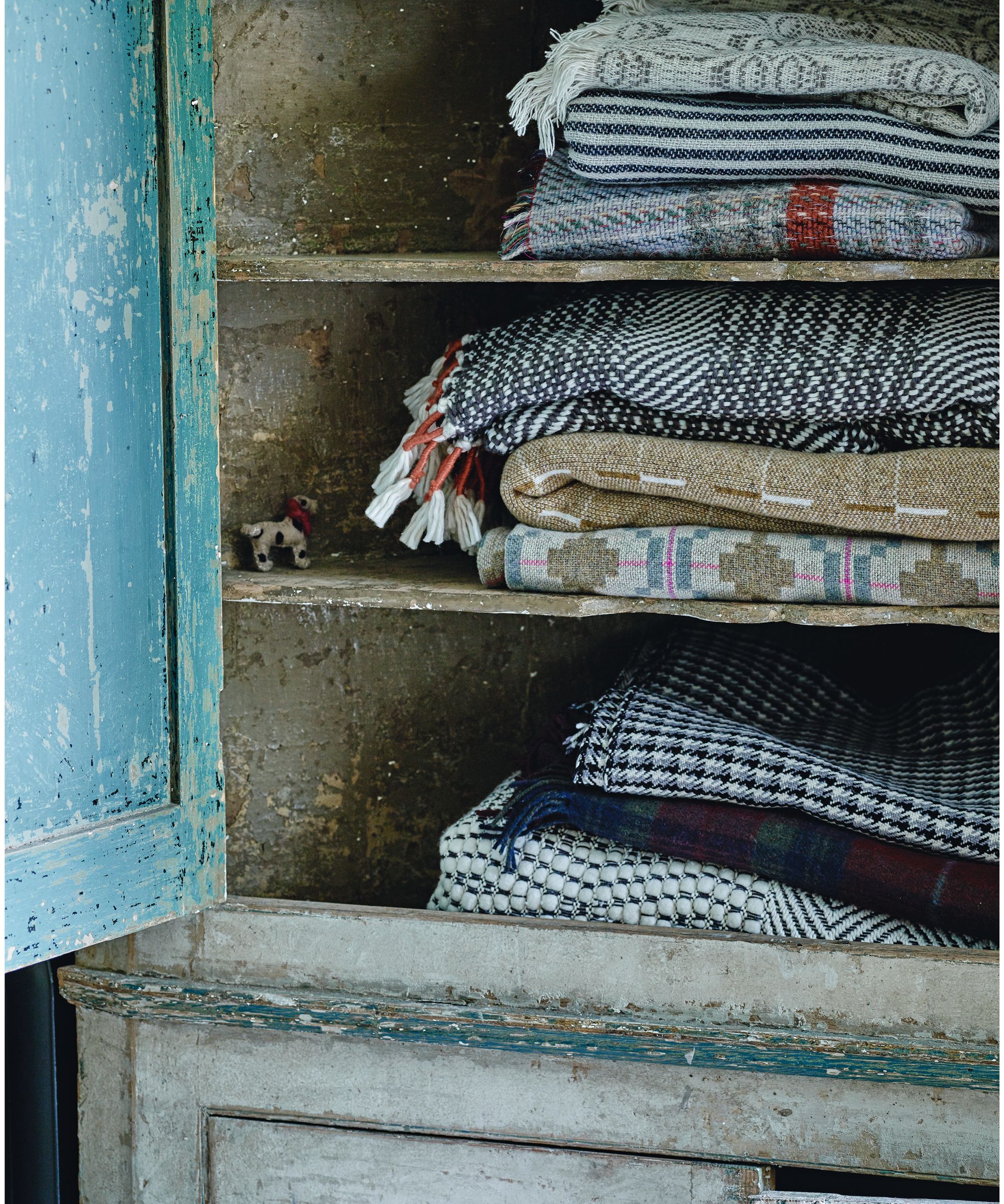 An open blue cupboard filled with patterned blankets