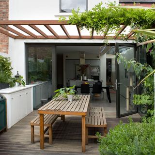 garden decking area with wooden dinning table and bench plants