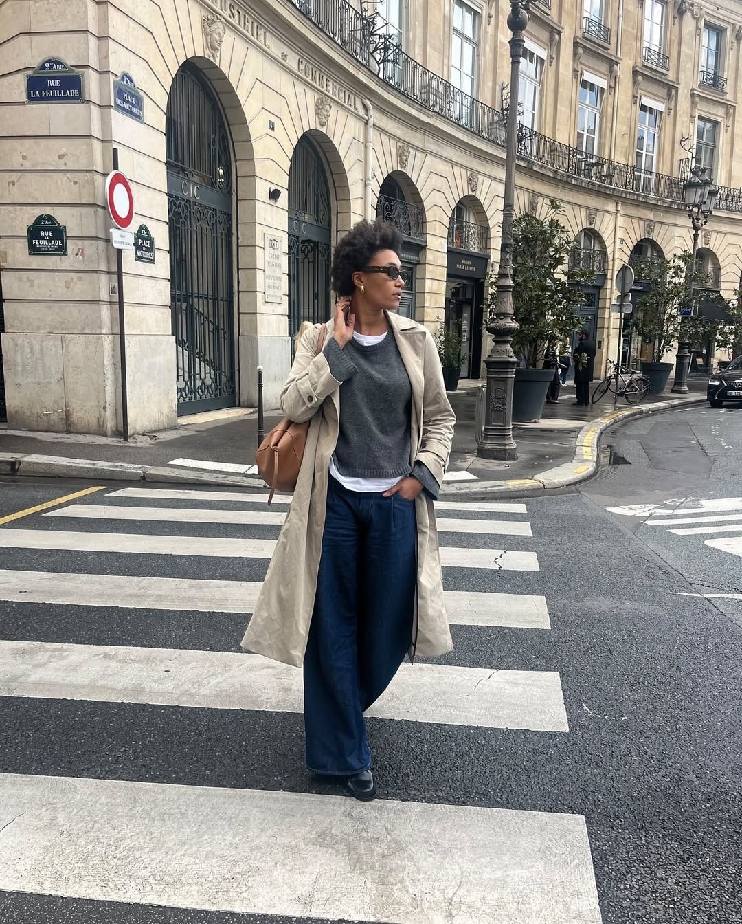 Parisian content creator Léna Farouil steps out in a wide-leg jean, layered white tee and heather grey crewneck, and French woman staple, a trench coat.