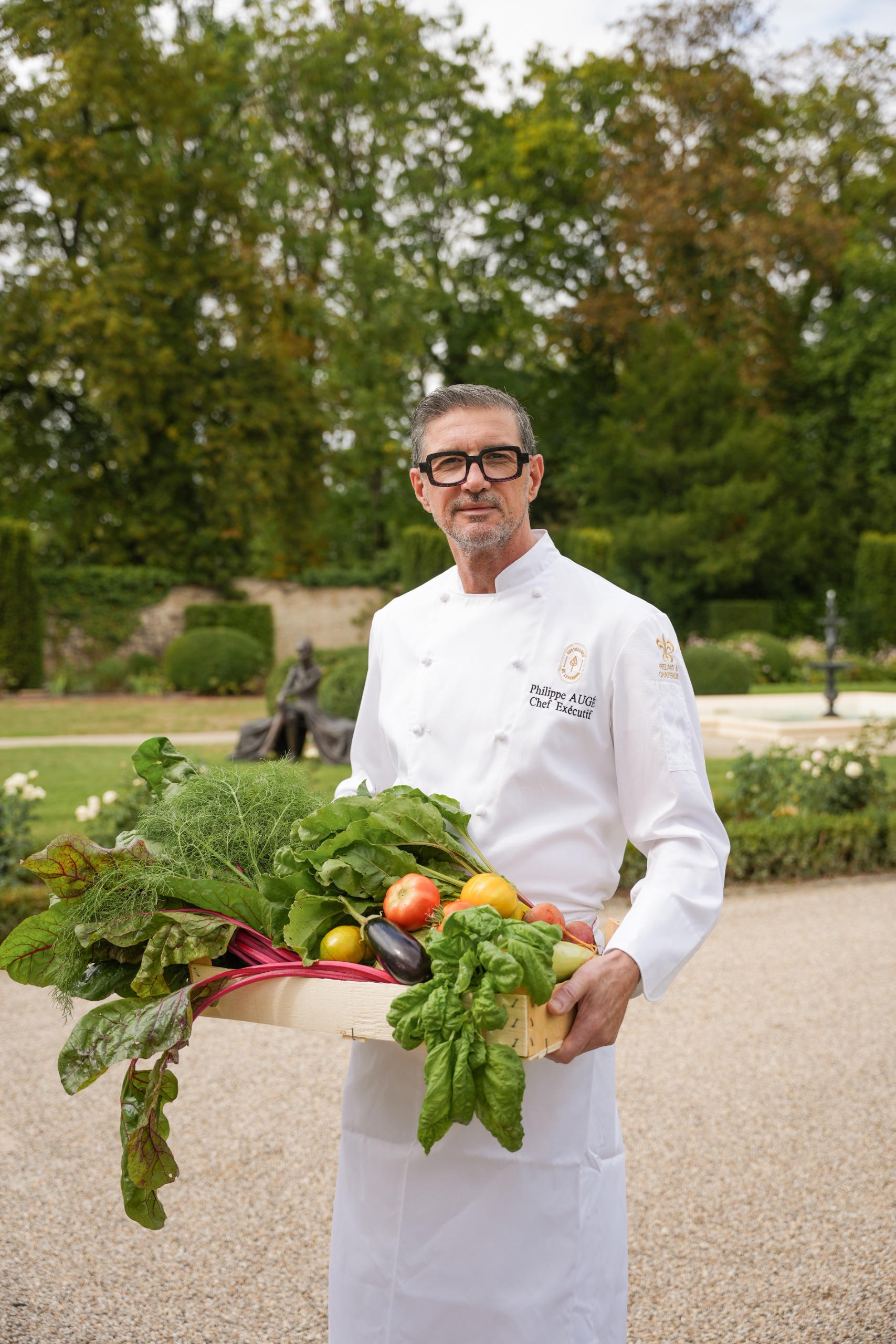 Man in chef's whites holding a tray of freshly harvested vegetables
