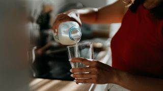 A close-up of a person pouring milk out of a plastic bottle into a glass in a kitchen.