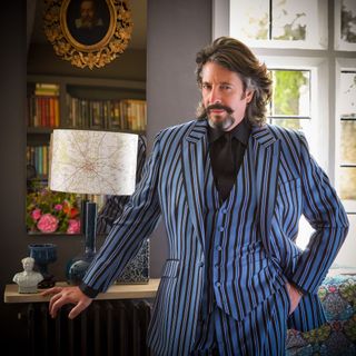 Laurence Llewelyn-Bowen standing beside a console table and lamp