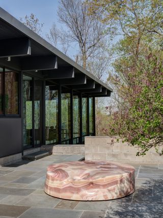 Modernist glass and steel house with stone floor terrace displaying round marble sculpture