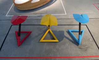 View of 'Bank Shovel' by Leo Capote - three stools with shovel seats and triangle bases in red, yellow and blue colours