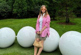 Nikki Chwatt wears green bermuda shorts from Zara, a pink striped button-down, white button-down, yellow sunglasses and a straw shoulder bag.