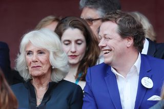 Tom Parker Bowles sitting next to his mother The Queen laughing and smiling while wearing a blue suit