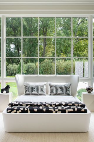 Windows behind bed with white curved bedhead and black and white bedding