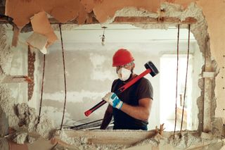 A man holding a sledgehammer behind a hole in the wall