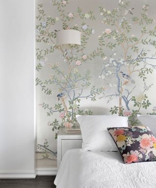 Bedroom with elaborate silver and floral wallpaper, dark wooden flooring and double bed with white bedlinen and colourful cushions.