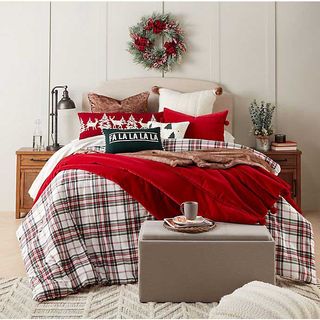 A bedroom with white wall panel wall decor, Christmas garland, textured cream carpet, tartan red, white and black duvet and various Christmas themed cushions