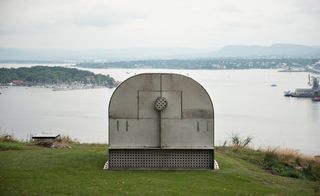 A grey metal scu;ture on an high open fields with view of the ocean