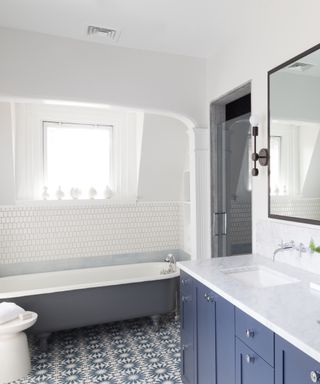 Blue bathroom with white walls, blue tub, patterned floor, blue cabinetry, wall tiles, white walls and ceiling