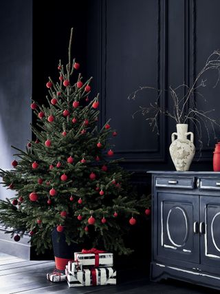 A hallway with black wall and floor paint decor with Christmas tree decorated exclusively with red baubles