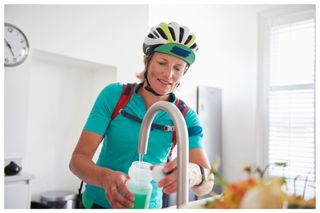 A female cyclist fills her water bottle from her kitchen tap