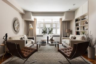 A living room with a light neutral palette, two leather accent chairs, and two cream sofas facing each other
