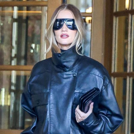 Rosie Huntington Whitely wearing a leather funnel-neck jacket with barrel leg trousers, heels, a clutch, and oversized sunglasses outside of the Ritz Hotel in Paris during Paris Fashion Week. 